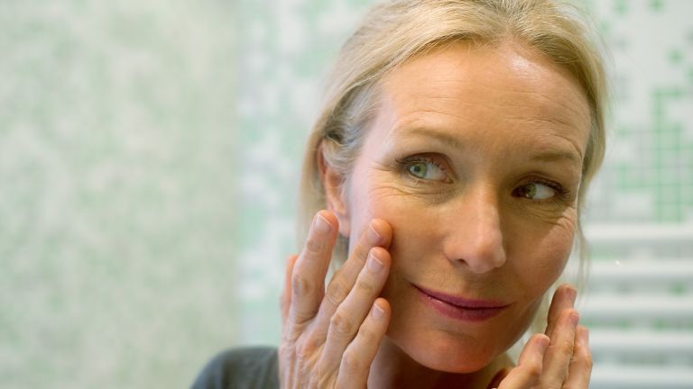 Reife Frau, die Reflexion im Spiegel mit der Hand auf der Wange betrachtet - Stock-Fotografie