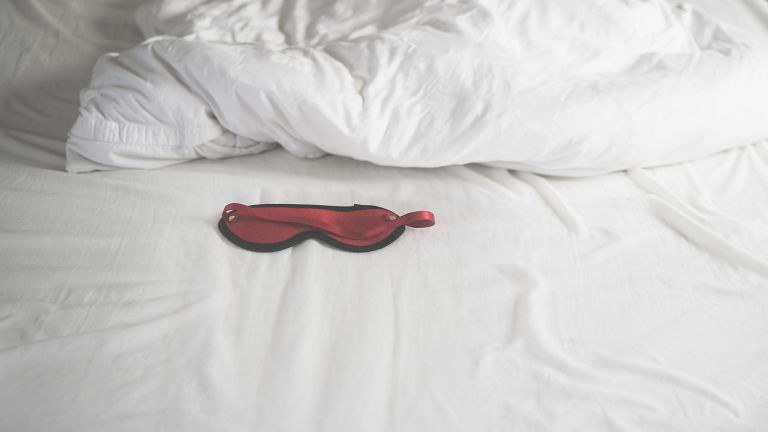 geheime Vibratoren, rote Seiden-Augenmaske auf dem Bett