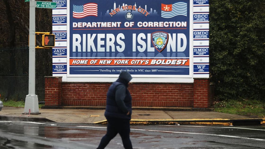 Una mujer pasa junto a un cartel a la entrada de Rikers Island.