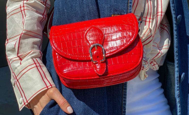 Julia Comil nosi belo in rdečo srajco znamke Brock Collection, modro jakno iz jeansa znamke Brock Collection, bele kavbojke iz jeansa znamke J Brands, rdečo usnjeno vintage torbo čez telo znamke Longchamp, med spletno modno fotografijo na daljavo prek Apple iphone / Facetime in aplikacija CLOS kot model ima sedež v Los Angelesu v Kaliforniji, fotograf pa v Parizu v Franciji, 27. marca 2021 v Parizu v Franciji.