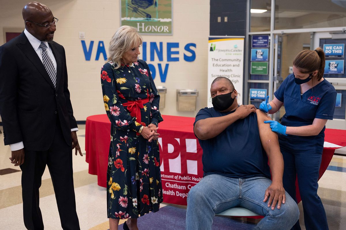 A primeira-dama dos EUA, Jill Biden, acompanha o senador dos EUA Raphael Warnock (L), D-GA, enquanto Alfred Lee Smith (C) é vacinado com a vacinação COVID-19 da Johnson & Johnson em um centro de vacinação na Alfred E. Beach High School em Savannah, Geórgia, em 8 de julho de 2021.