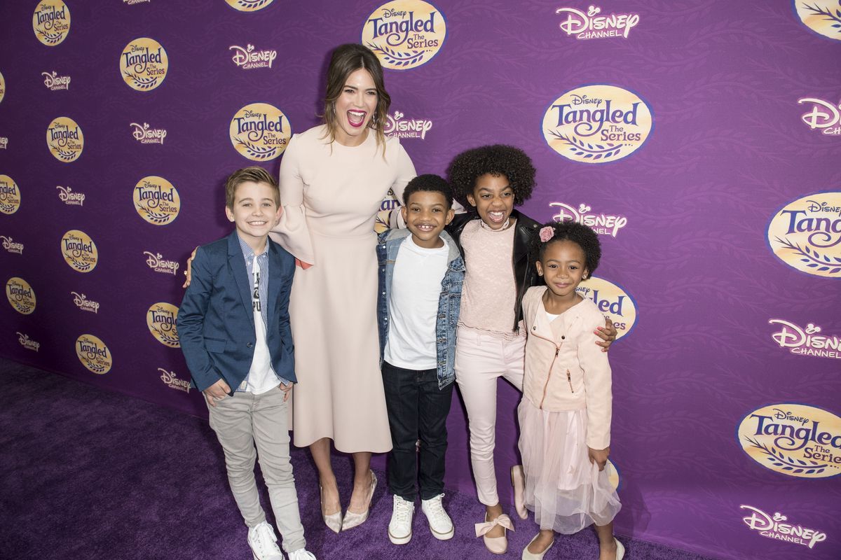 Mandy Moore se tient avec quatre enfants devant un panneau Tangled