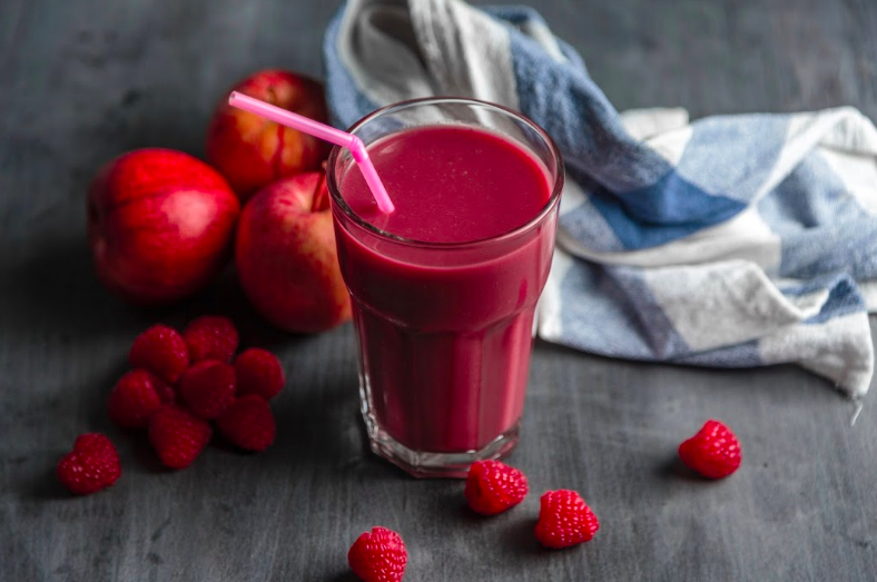 Jablkové, bobuľové a mätové smoothie v pohári s ružovou slamkou a bobuľami a jablkom rozhádzaným po pohári