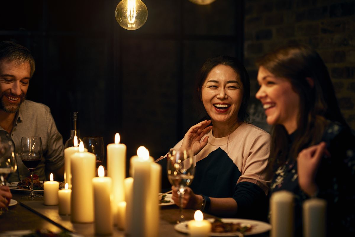 Amigos se reunindo para jantar em um restaurante, compartilhando ideias de presentes de 40 anos em torno de velas e taças de vinho na mesa
